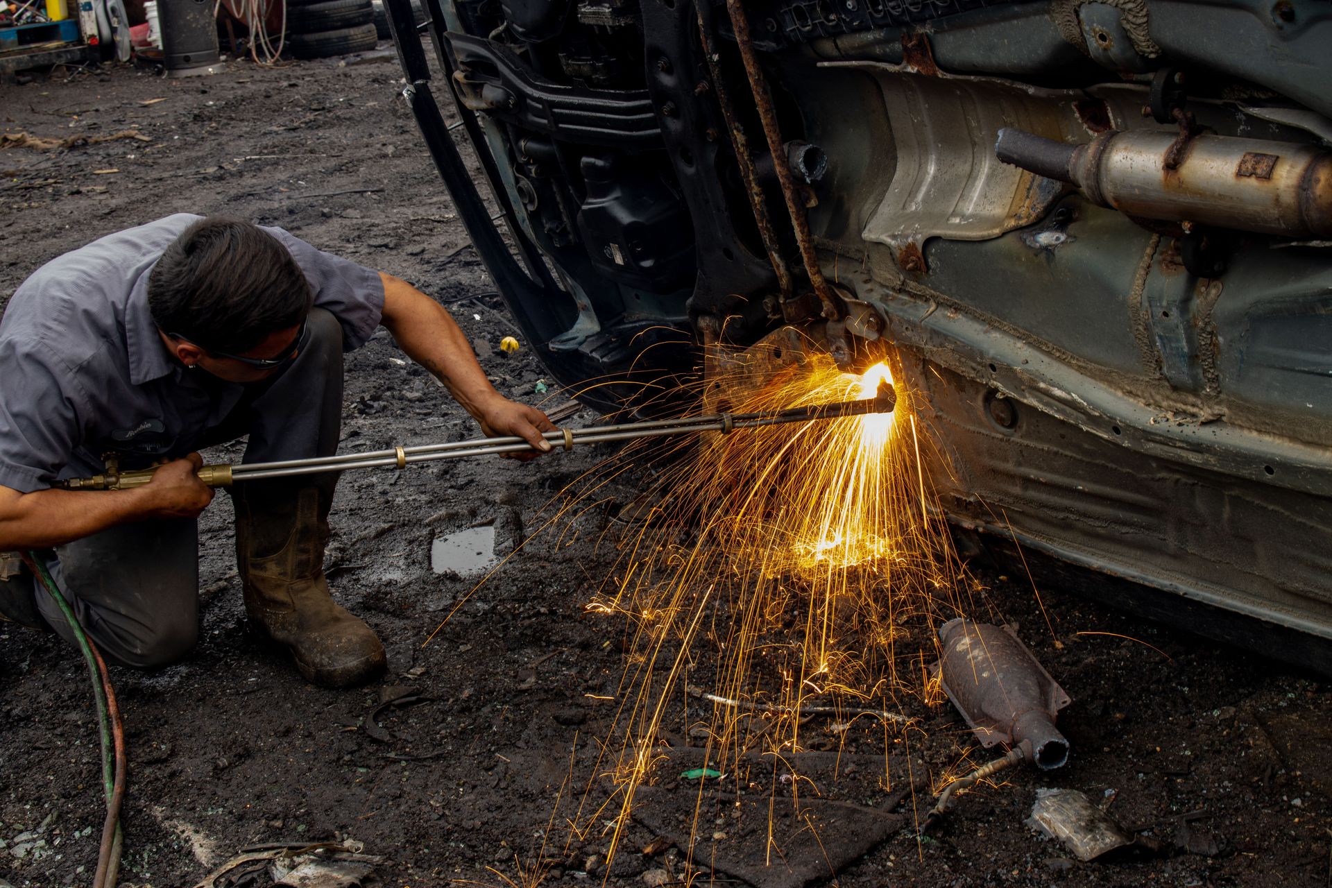 Mechanic welding a car frame outdoors, producing dramatic sparks and intense focus.
