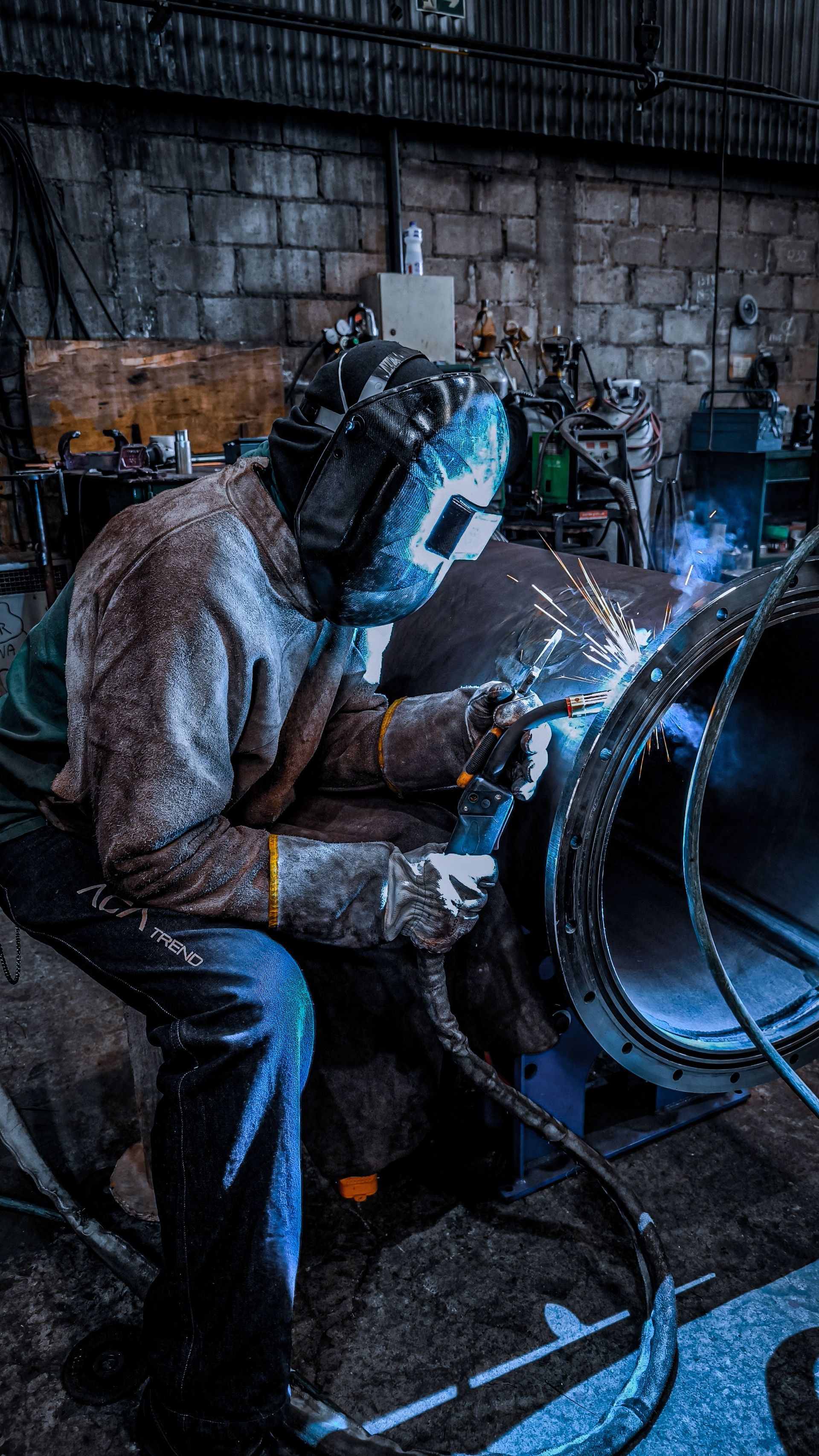 A worker welding inside a factory in Brazil, wearing safety gear and helmet.