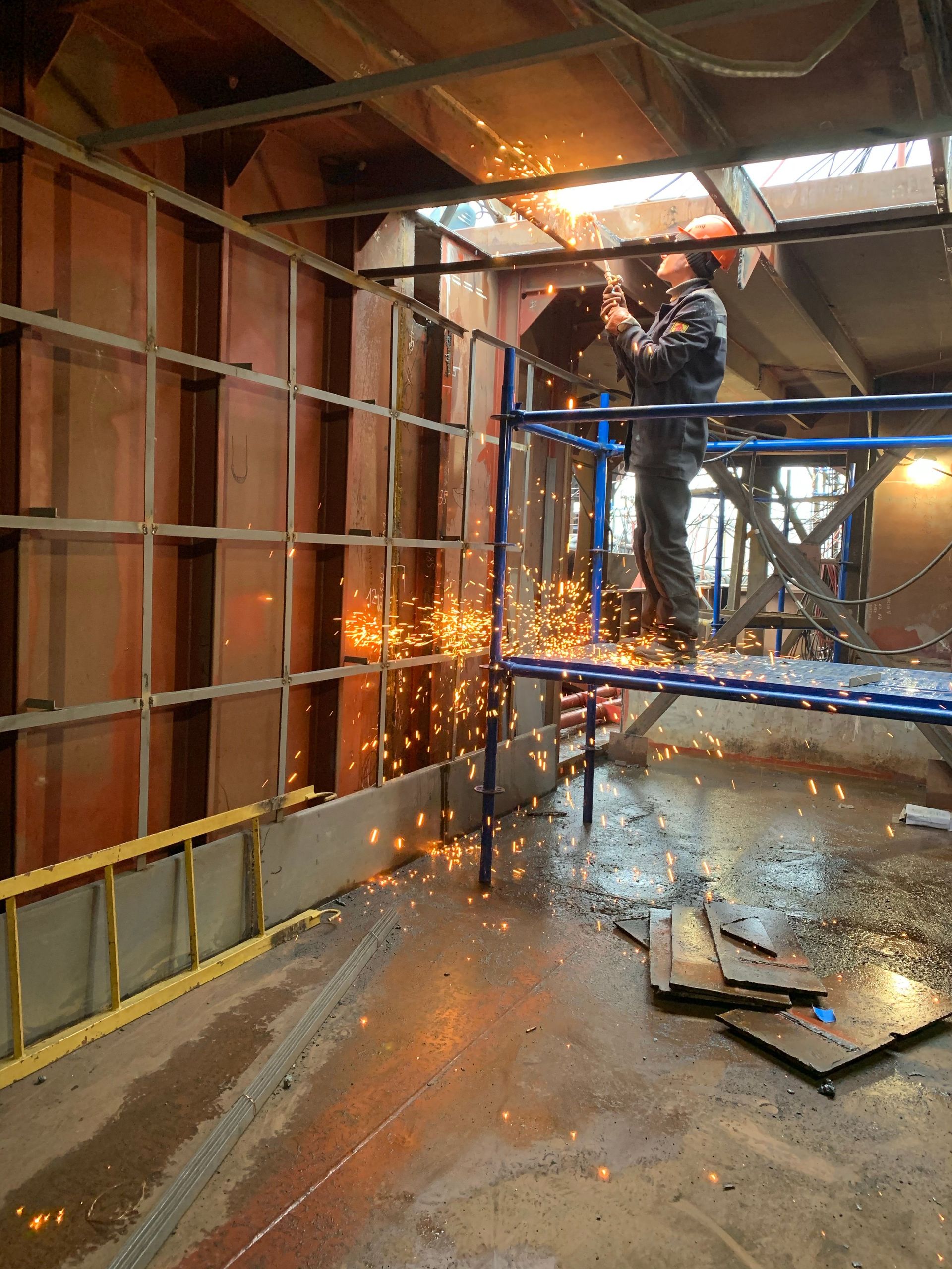 Side view of professional male worker in workwear and gloves helmet welding metal construction while installing ceiling inside industrial building